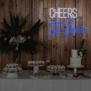blue cheers to love neon sign hanging above dessert table