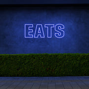 blue eats neon sign hanging on outside wall