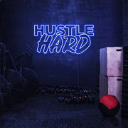 blue hustle hard neon sign hanging on gym wall
