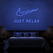 blue just relax neon sign hanging on bedroom wall