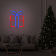 blue Christmas present neon sign hanging on lounge room wall next to Christmas tree