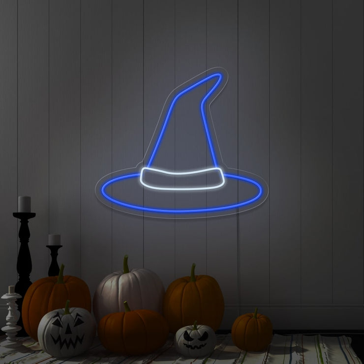 blue witch hat neon sign hanging on wall above pumpkins