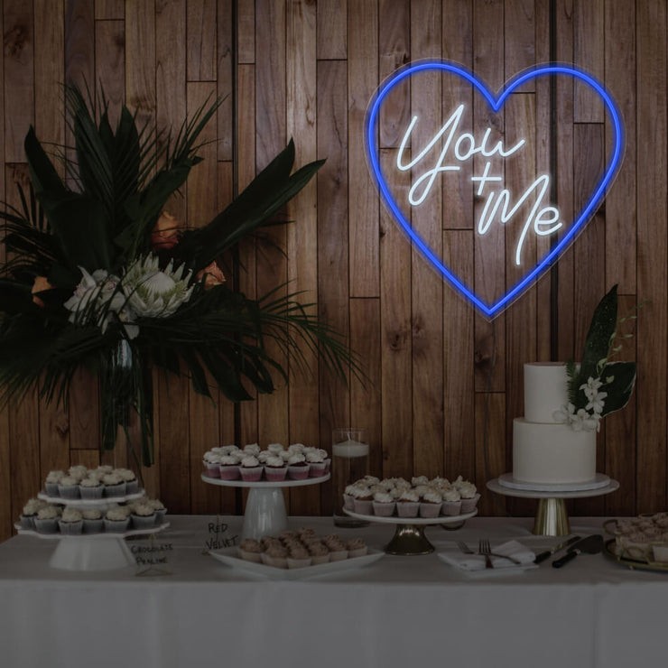 blue you and me neon sign hanging on timber wall above dessert table