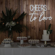 cold white cheers to love neon sign hanging above dessert table