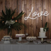 cold white love neon sign hanging on timber wall above dessert table