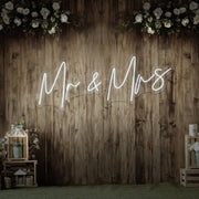 cold white mr and mrs neon sign hanging on wall with flowers