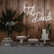 cold white til death neon sign hanging on timber wall above dessert table
