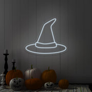 cold white witch hat neon sign hanging on wall above pumpkins
