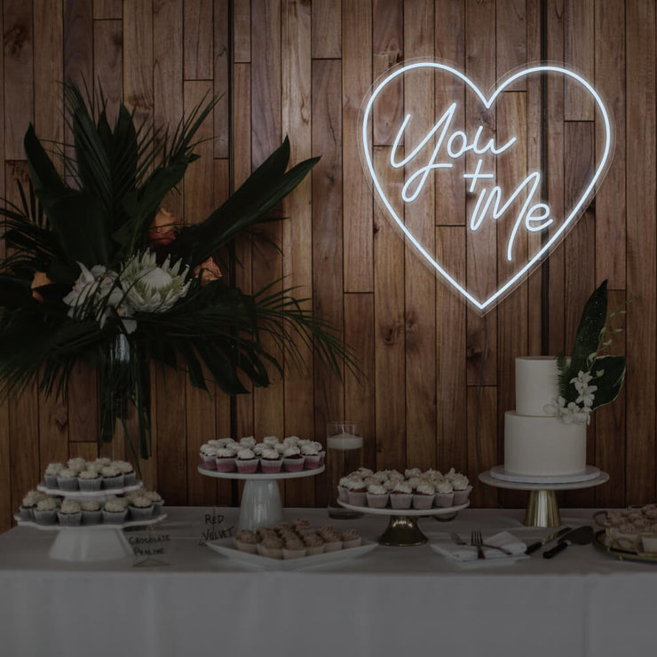 cold white you and me neon sign hanging on timber wall above dessert table