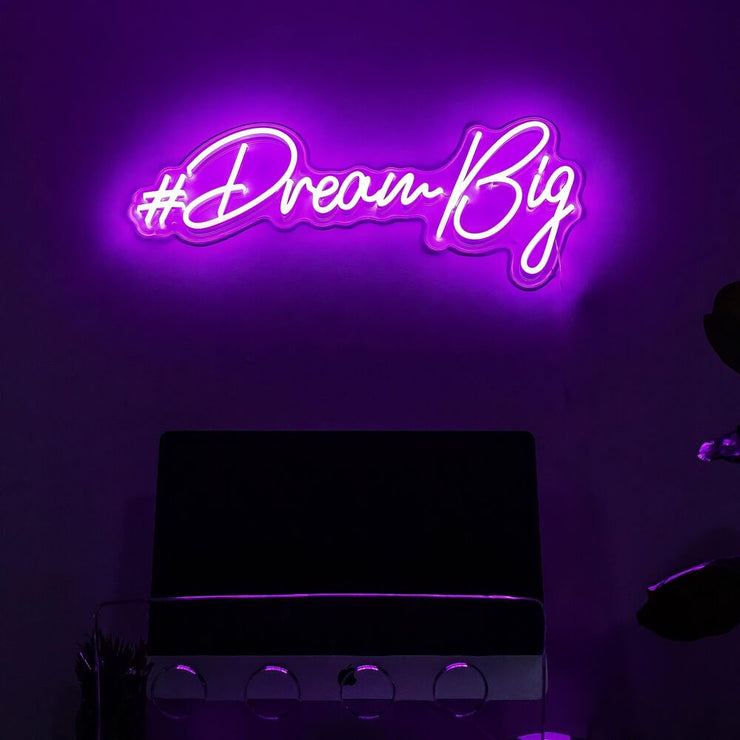 purple dream big neon sign hanging on office wall above computer