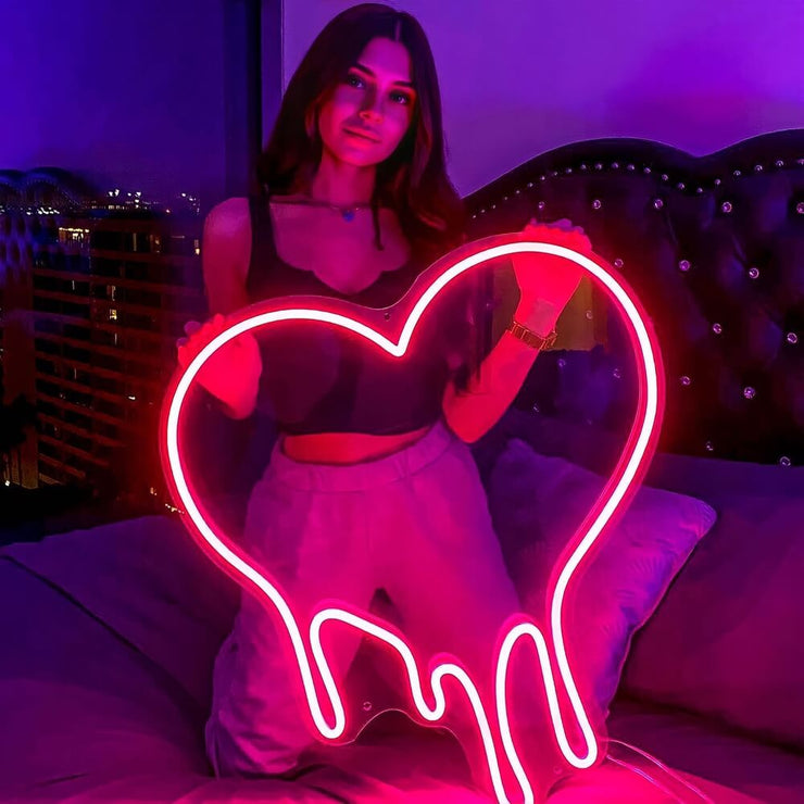 girl holding pink melting heart neon sign on bed