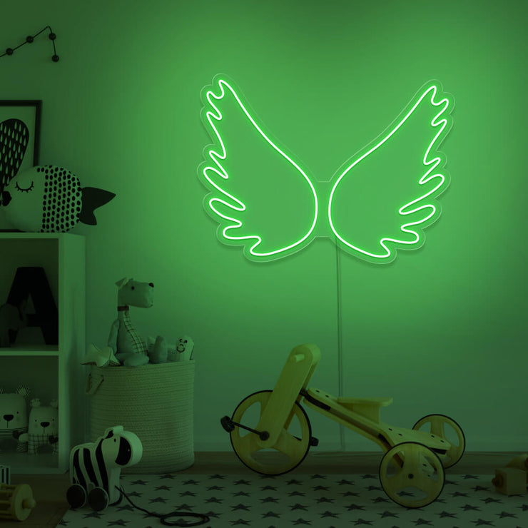 green angel wings neon sign hanging on kids bedroom wall