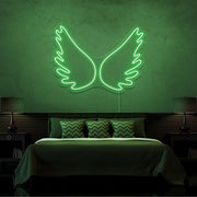 green angel wings neon sign hanging on bedroom wall