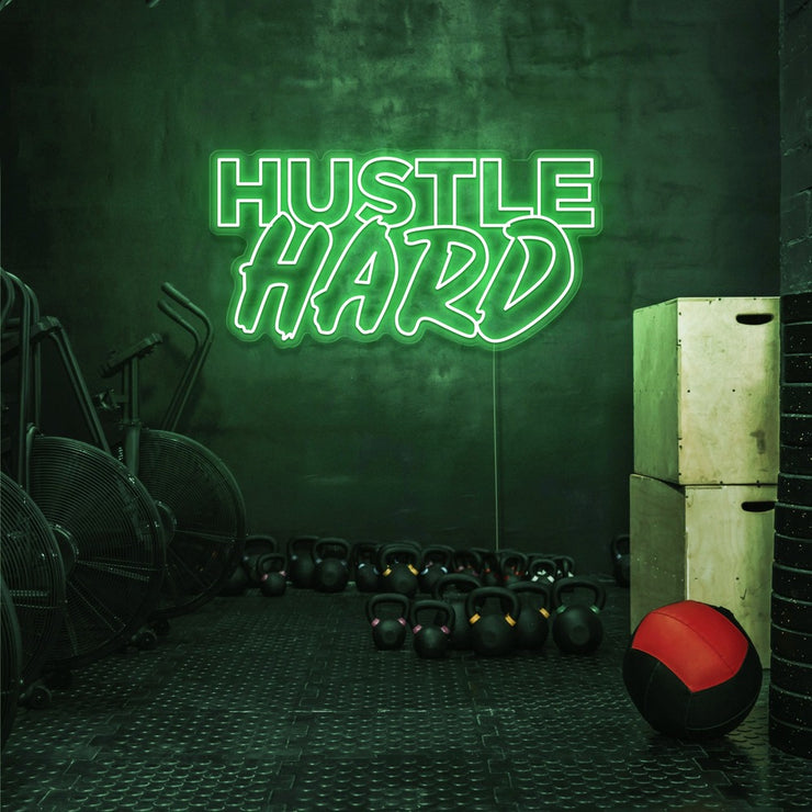 green white hustle hard neon sign hanging on gym wall