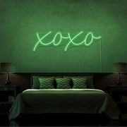 green xoxo neon sign hanging on bedroom wall