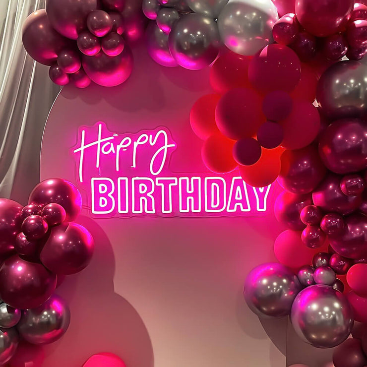 pink happy birthday neon sign on backdrop with balloon garland