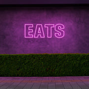 hot pink eats neon sign hanging on outside wall