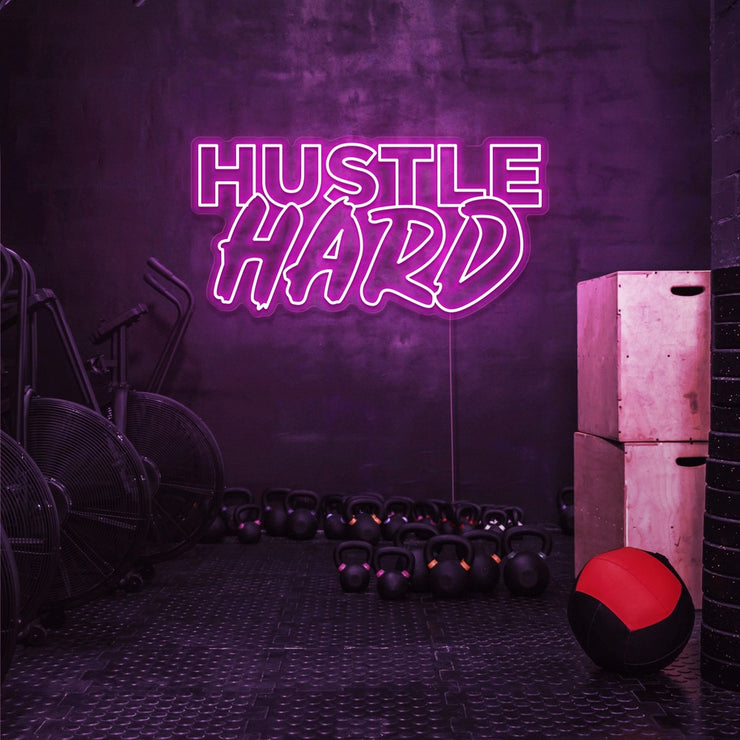 hot pink hustle hard neon sign hanging on gym wall