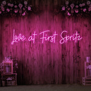 hot pink love at first spritz neon sign hanging on timber wall