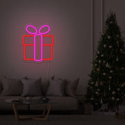 hot pink Christmas present neon sign hanging on lounge room wall next to Christmas tree