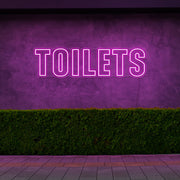 hot pink toilets neon sign hanging on outdoor wall
