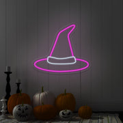hot pink witch hat neon sign hanging on wall above pumpkins