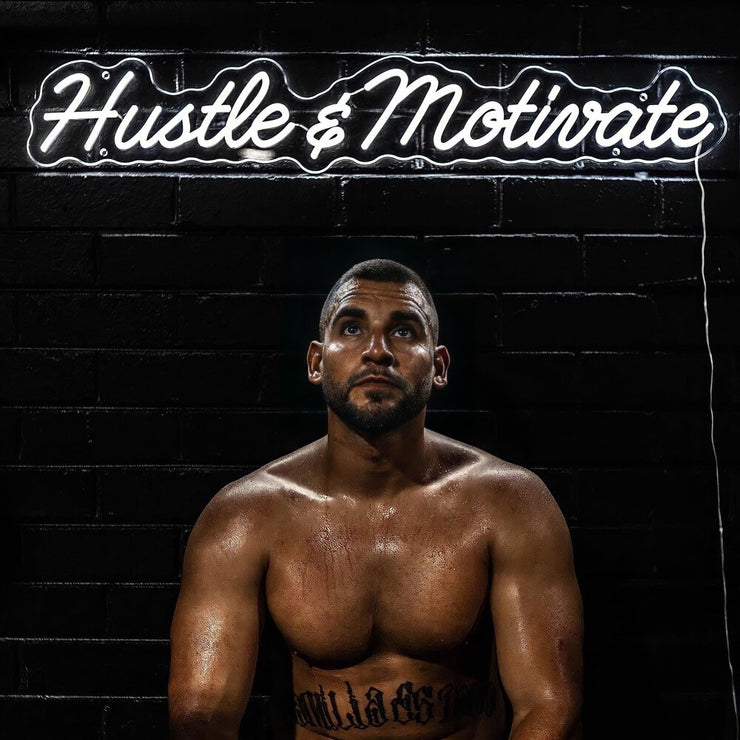 hustle and motivate gym neon sign hanging on black wall above boxer