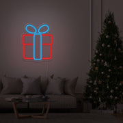ice blue Christmas present neon sign hanging on lounge room wall next to Christmas tree