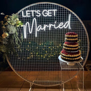 white lets get married neon sign hanging on white mesh backdrop frame