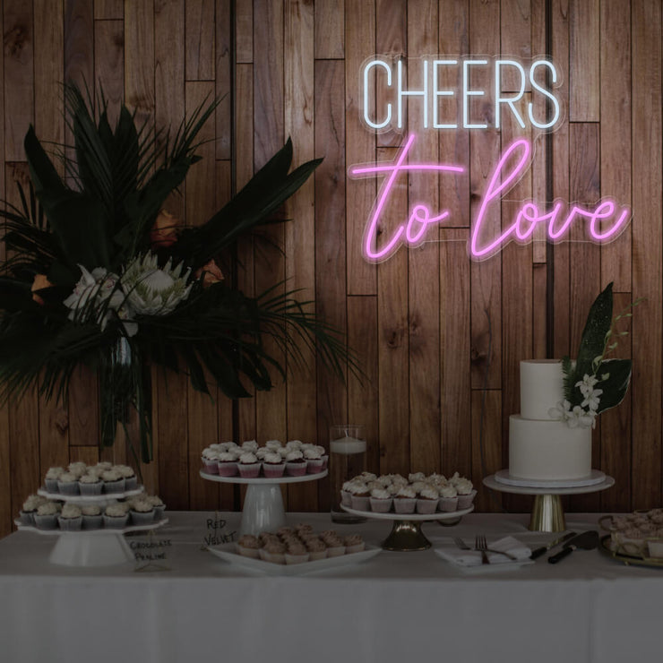 light pink cheers to love neon sign hanging above dessert table