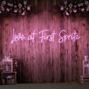 light pink love at first spritz neon sign hanging on timber wall