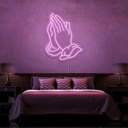 light pink praying hands neon sign hanging on bedroom wall