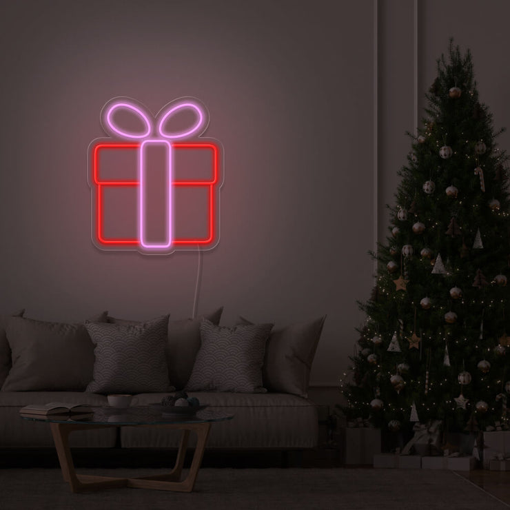 light pink Christmas present neon sign hanging on lounge room wall next to Christmas tree