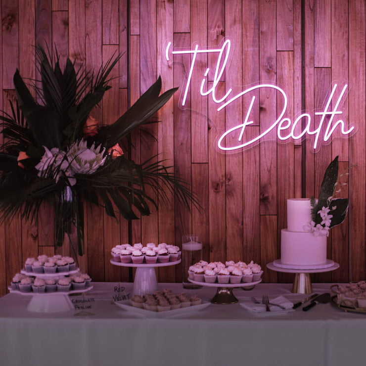 pink til death neon sign hanging on timber wall above dessert table