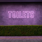 light pink toilets neon sign hanging on outdoor wall