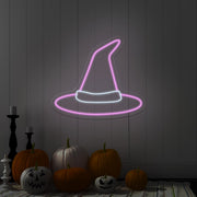 light pink witch hat neon sign hanging on wall above pumpkins