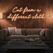 orange cut from a different cloth neon sign hanging on living room wall