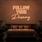 orange follow your dreams neon sign hanging on bedroom wall