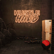 orange hustle hard neon sign hanging on gym wall