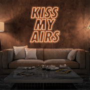 orange kiss my airs neon sign hanging on living room wall