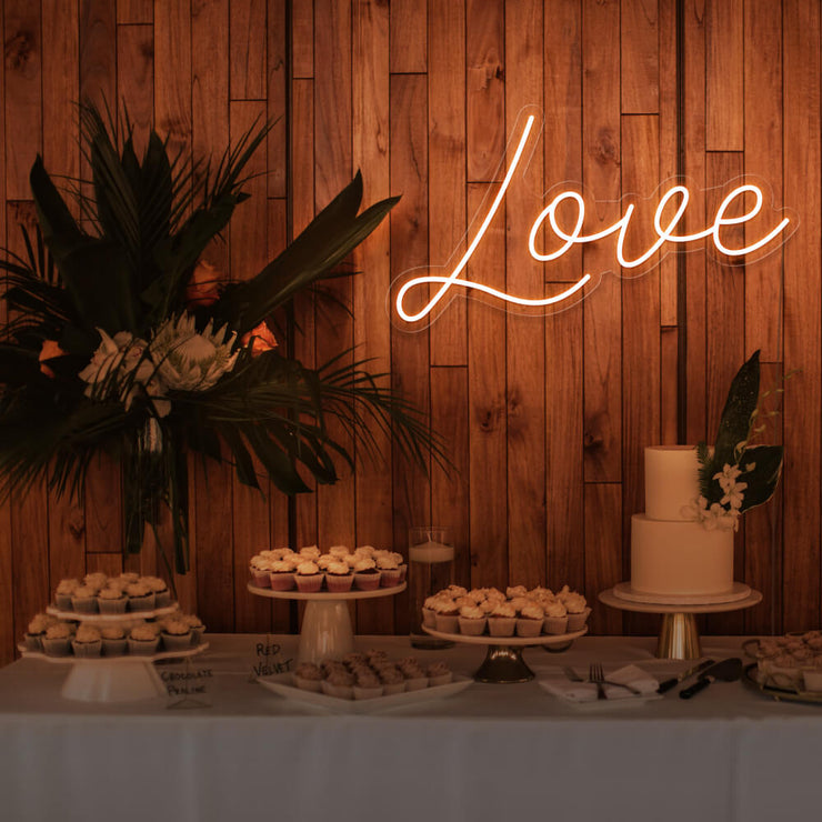 orange love neon sign hanging on timber wall above dessert table