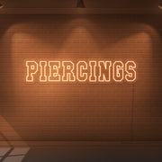 orange piercings neon sign hanging on wall