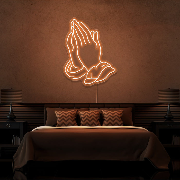 orange praying hands neon sign hanging on bedroom wall