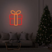 orange Christmas present neon sign hanging on lounge room wall next to Christmas tree