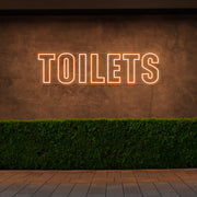 orange toilets neon sign hanging on outdoor wall