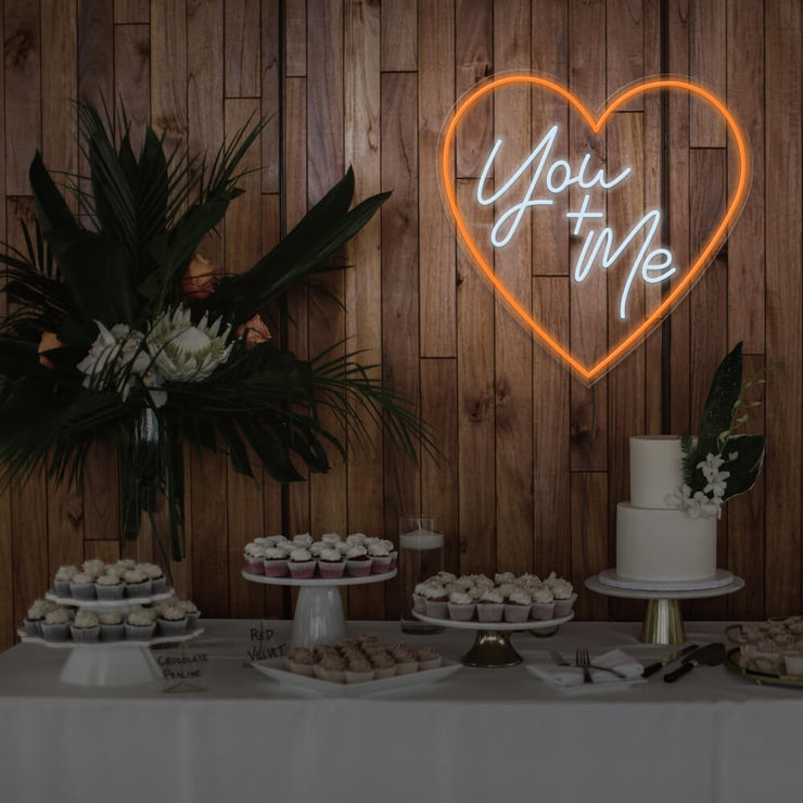 orange you and me neon sign hanging on timber wall above dessert table