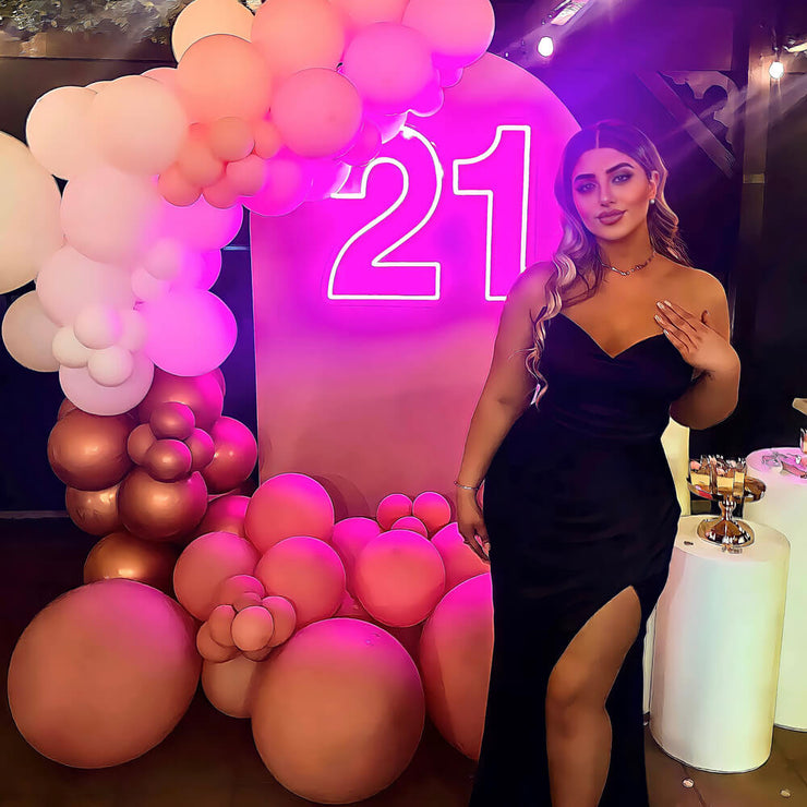 girl standing in front of hot pink 21 neon sign on backdrop wall with balloon garland