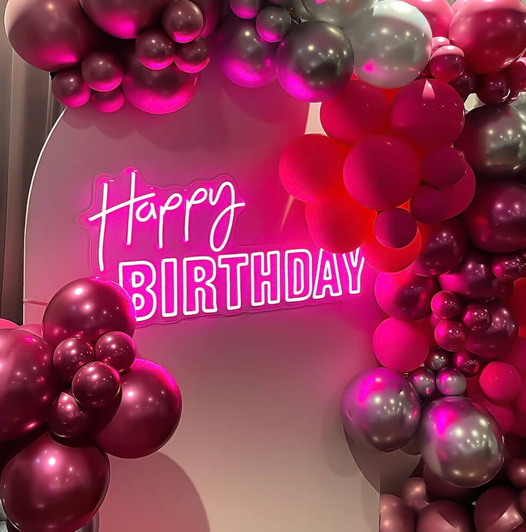 pink happy birthday neon sign on backdrop with balloon garland
