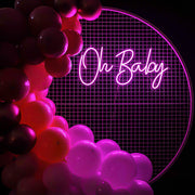 pink oh baby neon sign hanging on white mesh backdrop frame with balloons