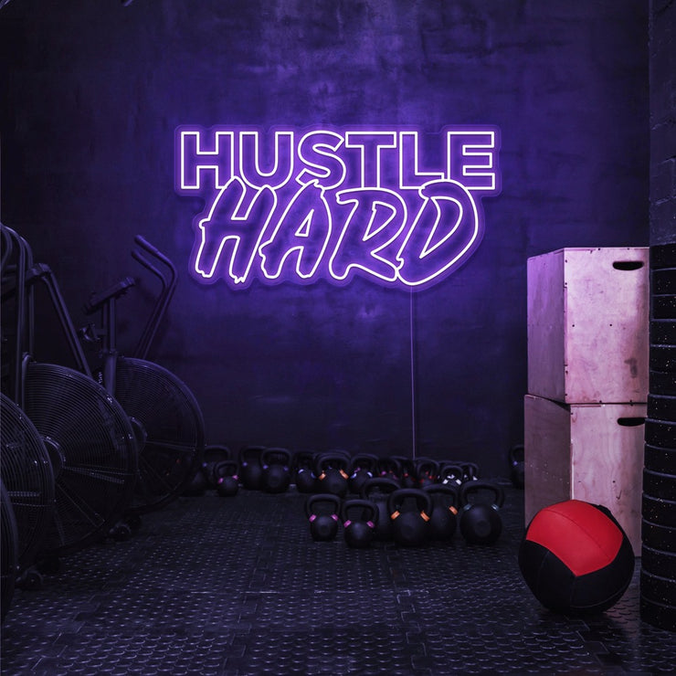 purple hustle hard neon sign hanging on gym wall
